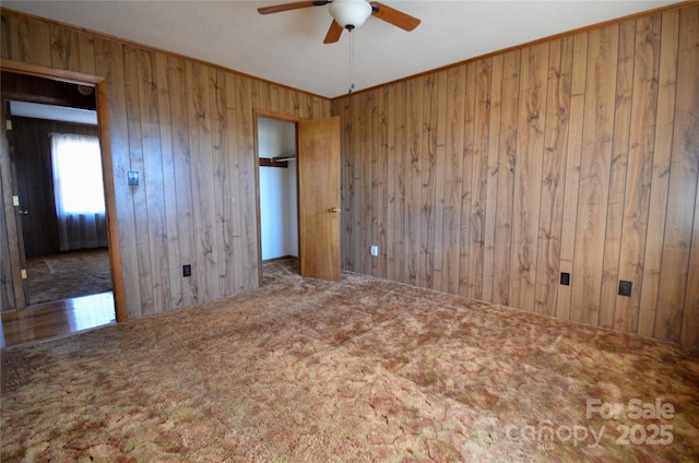 carpeted spare room with wooden walls, ornamental molding, and a ceiling fan