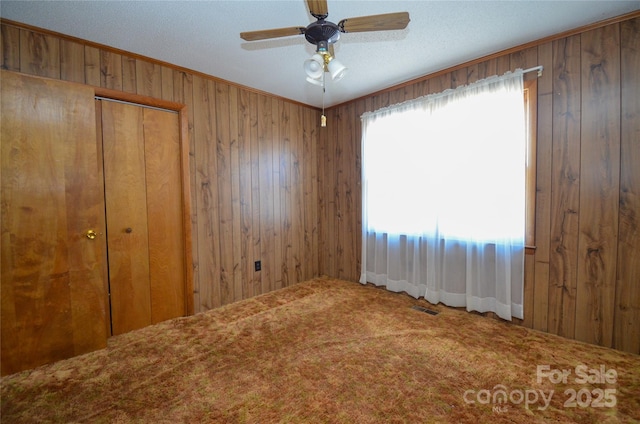 empty room featuring ornamental molding, wood walls, carpet flooring, and visible vents