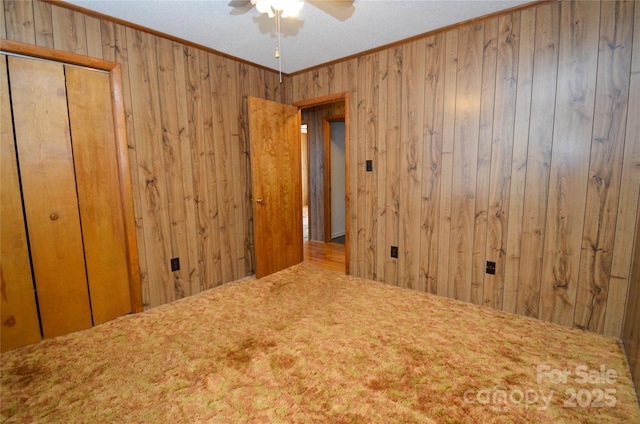 carpeted spare room with crown molding, wood walls, and ceiling fan