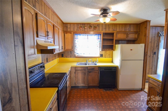 kitchen with black appliances, under cabinet range hood, a sink, and wood walls