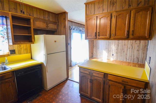 kitchen with black dishwasher, dark floors, wood walls, and freestanding refrigerator