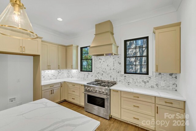 kitchen with a wealth of natural light, custom range hood, high end stainless steel range, and backsplash