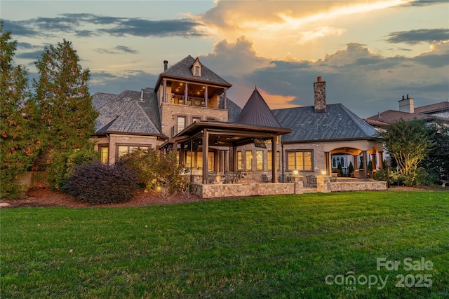 back house at dusk featuring a lawn and a patio