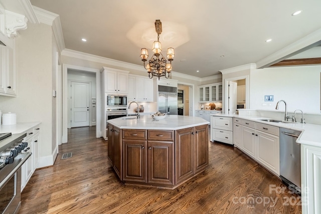 kitchen with sink, white cabinets, a kitchen island with sink, and built in appliances