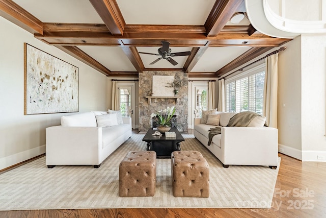 living room with a stone fireplace, light hardwood / wood-style floors, ceiling fan, beam ceiling, and coffered ceiling