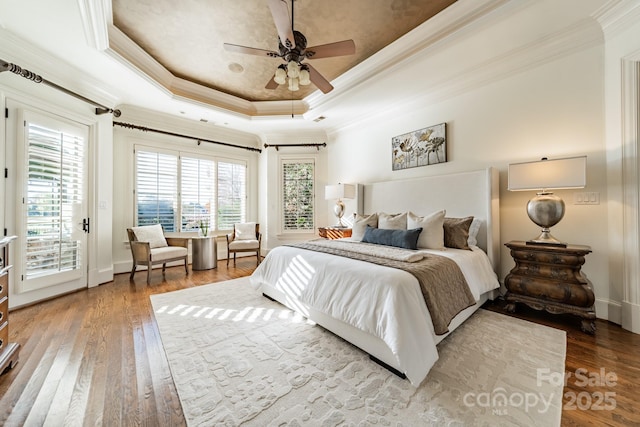 bedroom featuring hardwood / wood-style floors, access to outside, ceiling fan, a tray ceiling, and crown molding