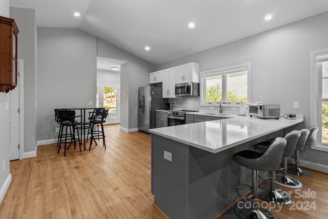 kitchen featuring white cabinetry, stainless steel appliances, light hardwood / wood-style floors, and vaulted ceiling