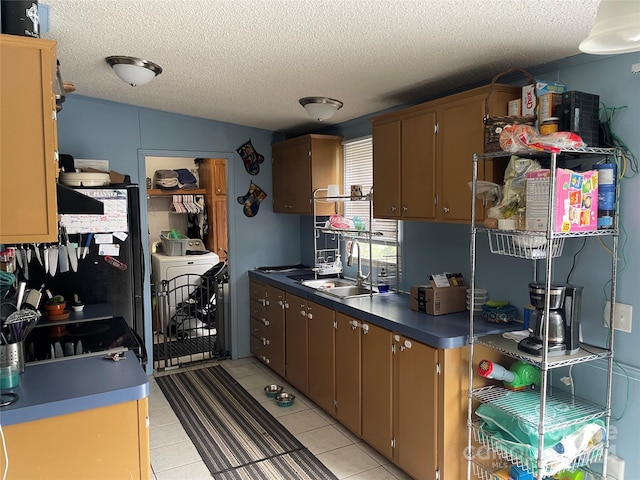 kitchen featuring stainless steel refrigerator, washer / dryer, sink, and a textured ceiling