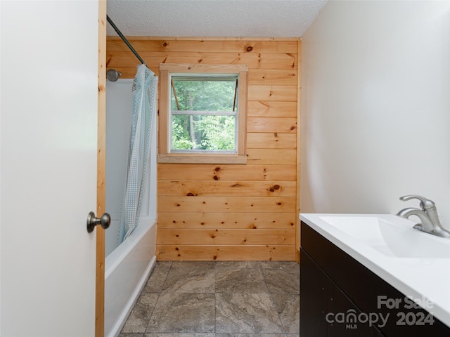 bathroom featuring shower / bath combo with shower curtain, wooden walls, vanity, and a textured ceiling