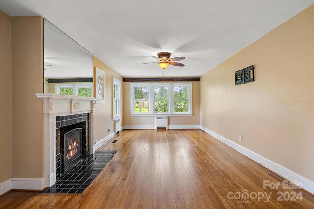 unfurnished living room featuring radiator heating unit, a fireplace, ceiling fan, and light hardwood / wood-style flooring