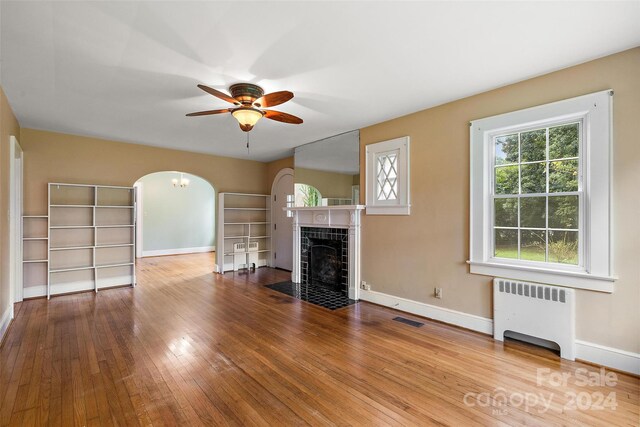 unfurnished living room featuring radiator heating unit, a fireplace, ceiling fan, and light hardwood / wood-style flooring