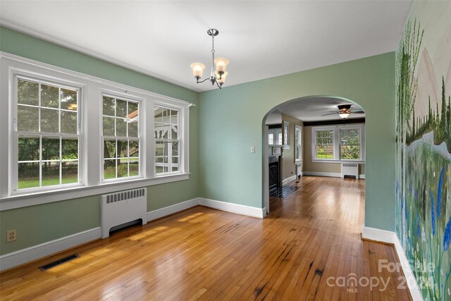 unfurnished dining area featuring ceiling fan with notable chandelier, light hardwood / wood-style floors, and radiator