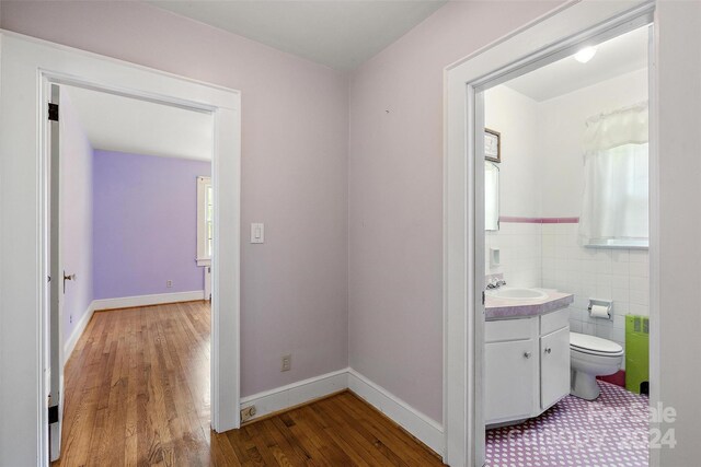 hall with sink, wood-type flooring, and tile walls