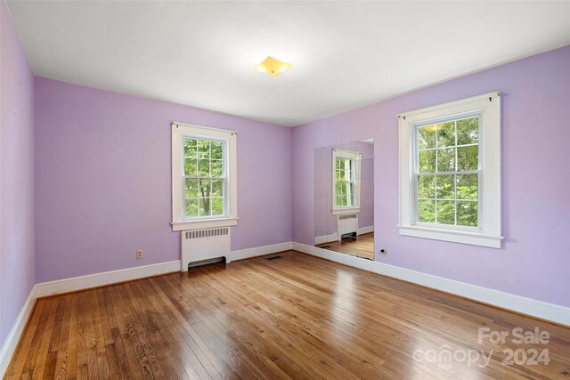 unfurnished room featuring a wealth of natural light, radiator heating unit, and light hardwood / wood-style floors