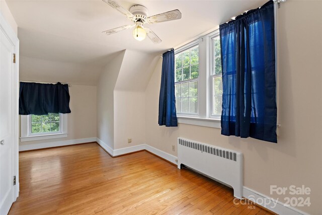 bonus room featuring light hardwood / wood-style floors, radiator heating unit, ceiling fan, and plenty of natural light