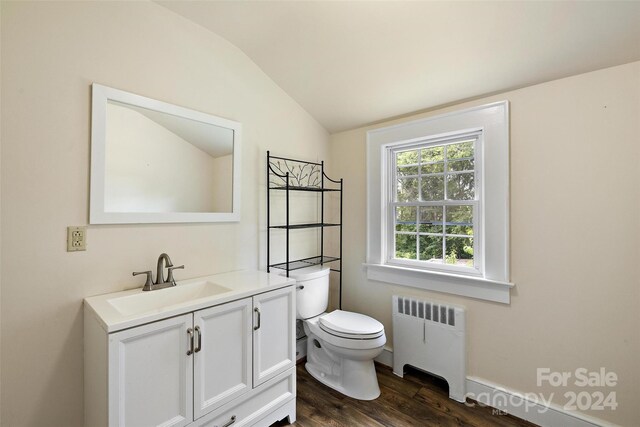 bathroom featuring vanity, hardwood / wood-style flooring, radiator, vaulted ceiling, and toilet