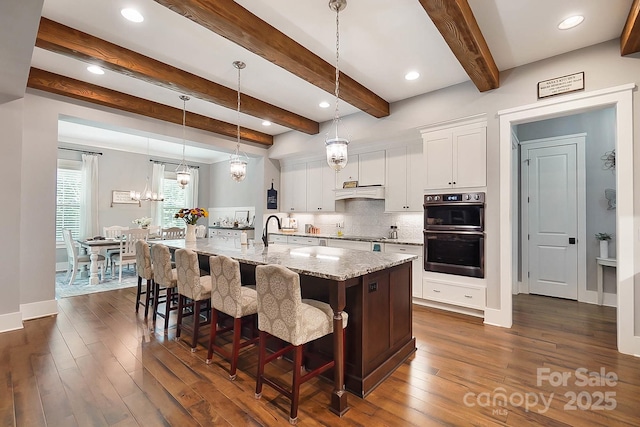 kitchen with a large island with sink, light stone countertops, white cabinets, and hanging light fixtures