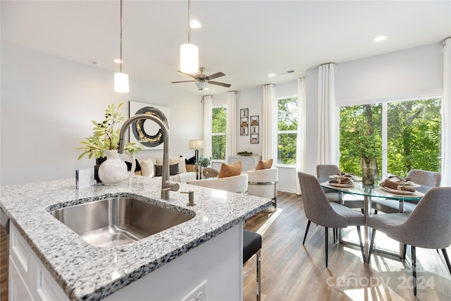 kitchen with sink, light stone counters, white cabinetry, hanging light fixtures, and light wood-type flooring