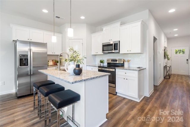 kitchen with white cabinetry, appliances with stainless steel finishes, hanging light fixtures, and a center island with sink