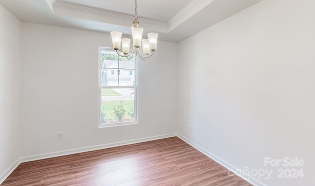 empty room with a chandelier, wood-type flooring, a tray ceiling, and ornamental molding