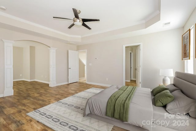 bedroom featuring crown molding, wood-type flooring, a tray ceiling, ceiling fan, and decorative columns