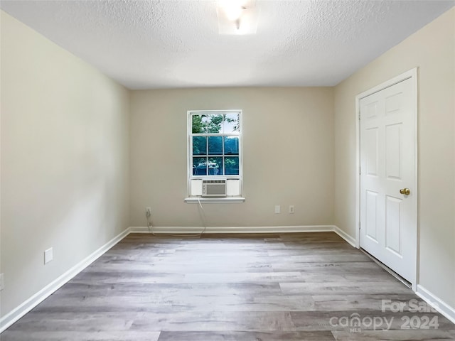 spare room with a textured ceiling, cooling unit, and light hardwood / wood-style flooring