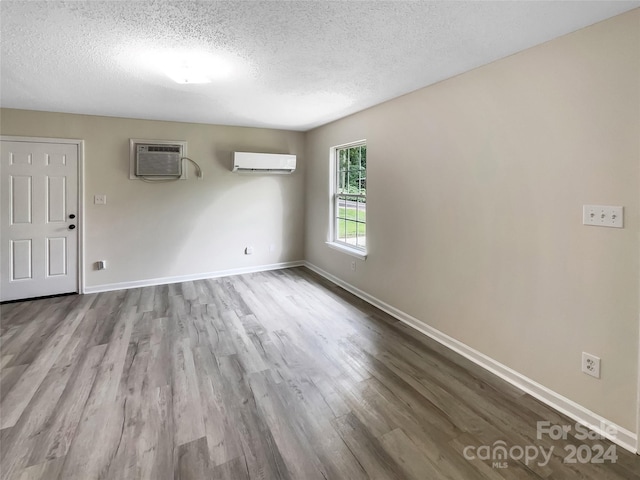 unfurnished room with hardwood / wood-style flooring, a textured ceiling, and a wall mounted air conditioner