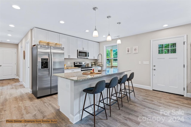 kitchen with light hardwood / wood-style floors, light stone counters, white cabinets, stainless steel appliances, and a kitchen island with sink