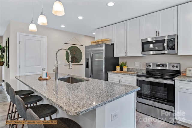 kitchen featuring an island with sink, decorative light fixtures, white cabinetry, appliances with stainless steel finishes, and light wood-type flooring