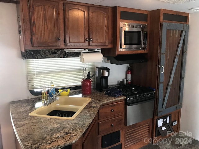 kitchen with stainless steel microwave, range with gas cooktop, dark stone counters, and sink