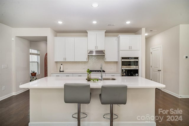 kitchen featuring sink, an island with sink, white cabinets, a breakfast bar, and dark hardwood / wood-style floors