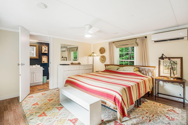 bedroom featuring light hardwood / wood-style floors, ensuite bath, ceiling fan, and a wall unit AC