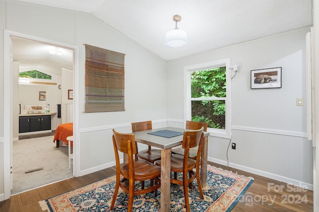 dining space featuring vaulted ceiling, a textured ceiling, and wood-type flooring