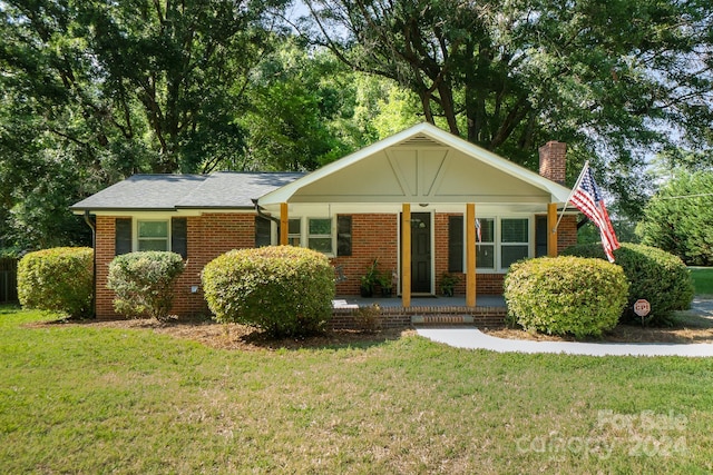 ranch-style home with a porch, brick siding, a chimney, and a front lawn