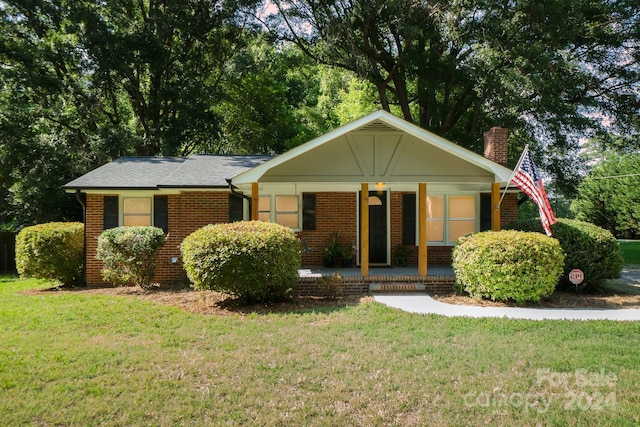 ranch-style house with covered porch, a chimney, a front lawn, and brick siding