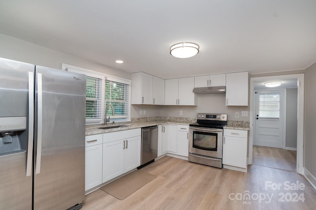 kitchen with appliances with stainless steel finishes, light stone countertops, under cabinet range hood, white cabinetry, and a sink