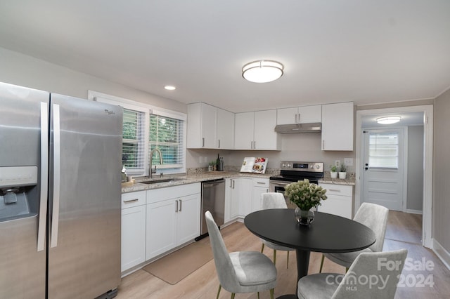 kitchen featuring light stone counters, appliances with stainless steel finishes, white cabinetry, a sink, and under cabinet range hood