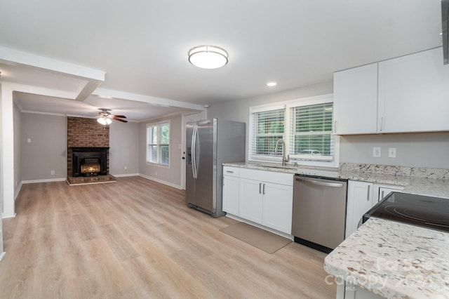 kitchen with light stone counters, stainless steel appliances, open floor plan, white cabinets, and a sink