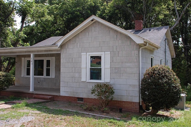 view of side of property with a shingled roof, a chimney, covered porch, and crawl space