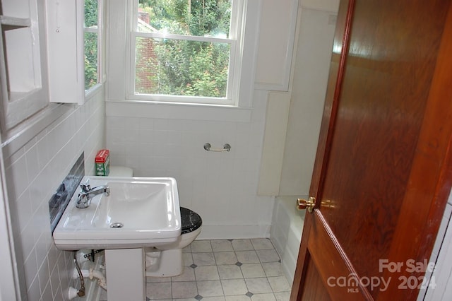 bathroom featuring tile walls, a washtub, tile patterned flooring, and toilet