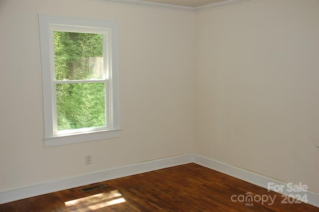 unfurnished room featuring dark wood-type flooring, visible vents, baseboards, and ornamental molding