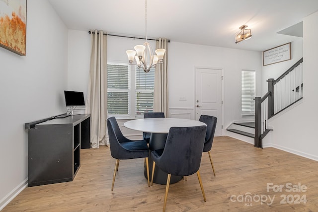 dining room featuring baseboards, stairway, light wood finished floors, and an inviting chandelier