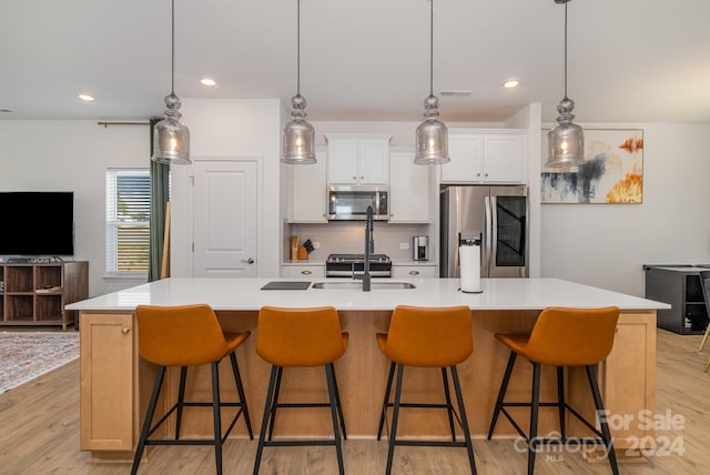 kitchen featuring decorative backsplash, a spacious island, stainless steel appliances, light wood-style floors, and a sink