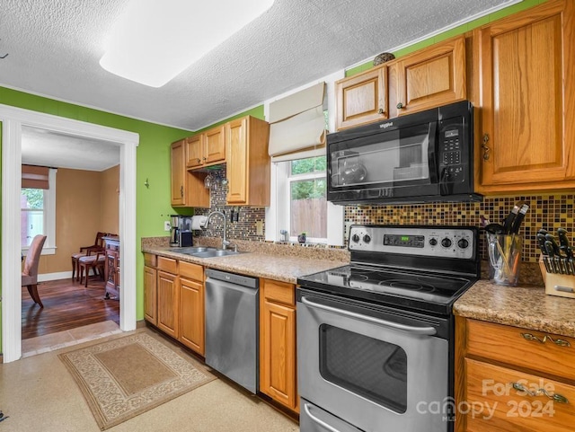 kitchen with a textured ceiling, stainless steel appliances, a sink, baseboards, and tasteful backsplash