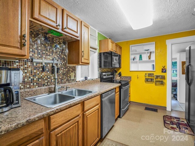 kitchen featuring a textured ceiling, light floors, a sink, visible vents, and black appliances