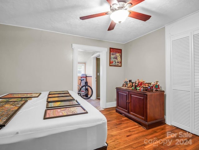 bedroom with a closet, a textured ceiling, ceiling fan, and wood finished floors