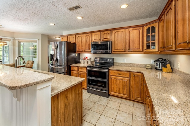 kitchen featuring a textured ceiling, light tile patterned floors, stainless steel appliances, light stone countertops, and a breakfast bar area