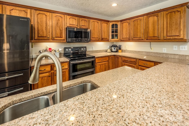 kitchen with appliances with stainless steel finishes, light stone countertops, sink, and a textured ceiling