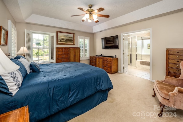 bedroom featuring ensuite bathroom, light colored carpet, a raised ceiling, ceiling fan, and a textured ceiling