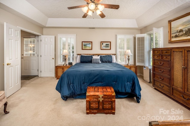 carpeted bedroom featuring multiple windows, ceiling fan, and a tray ceiling